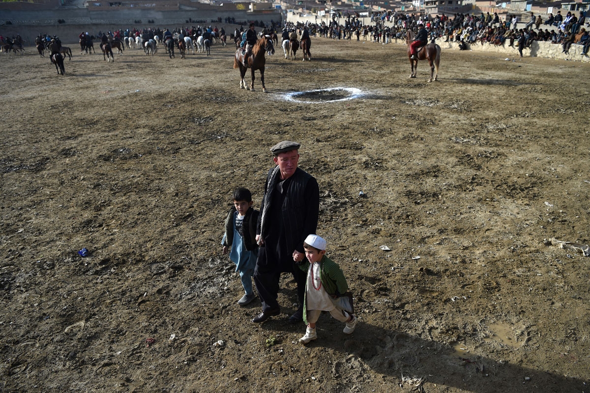 This photo taken on December 1, 2017 shows an Afghan man walking with children as horsemen compete in the traditional sport of buzkashi on the outskirts of Kabul.