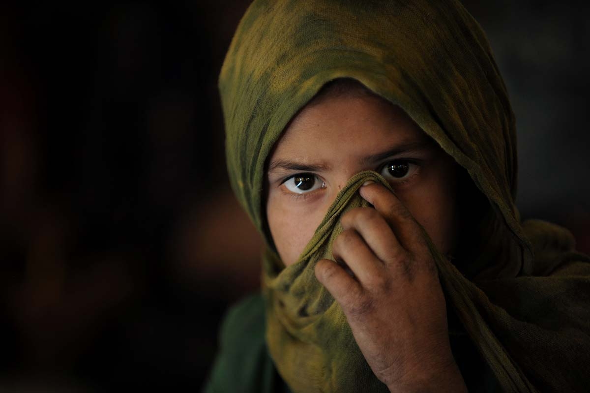 An Afghan Kuchi girl covers her face as she attends a class in a tent in front of the ruins of the Darlaman Palace which was destroyed during the civil war, on the outskirts of Kabul on October 27, 2010.
