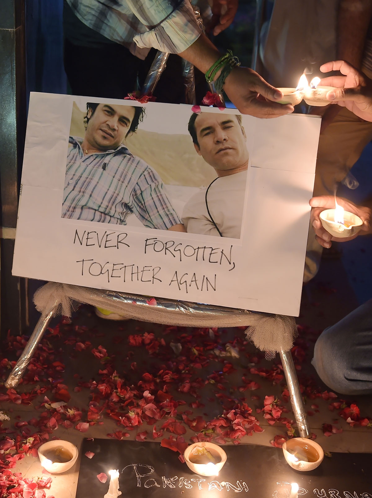Pakistani journalists light candles and oil lamps next to a photograph of Agence France-Presse (AFP) chief photographer for Afghanistan Shah Marai, who was killed along with other Afghan journalists in a targeted suicide bombing, during a vigil in Islamab
