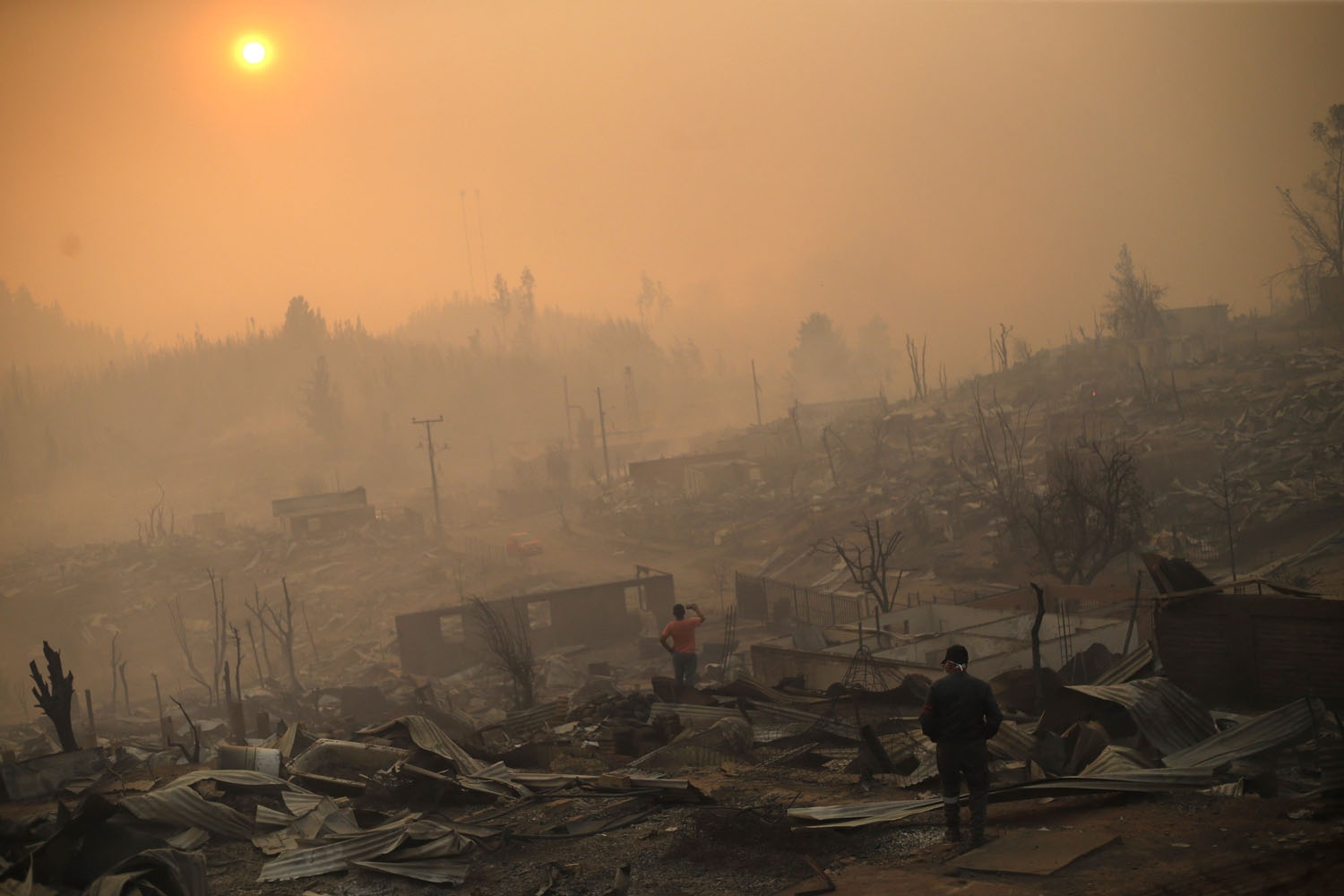 People walk amid the remains of burnt down buildings after a forest fire in Santa Olga, 240 kilometres south of Santiago, on January 26, 2017.