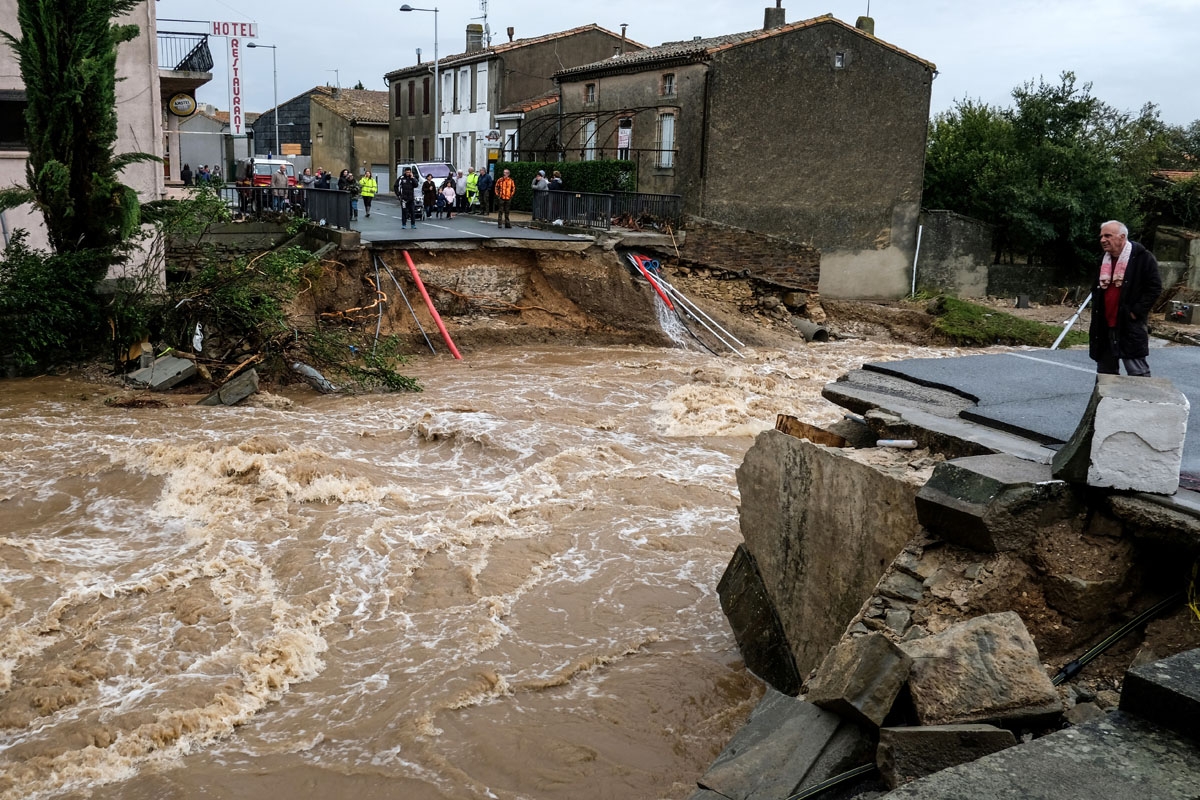 People stand on the road by a bridge over the Trapel river that collapsed Villegailhenc in the Aude department after it was particularly badly hit by heavy rain storms which swamped parts of southwestern France, flooding rivers and cutting roads, killing
