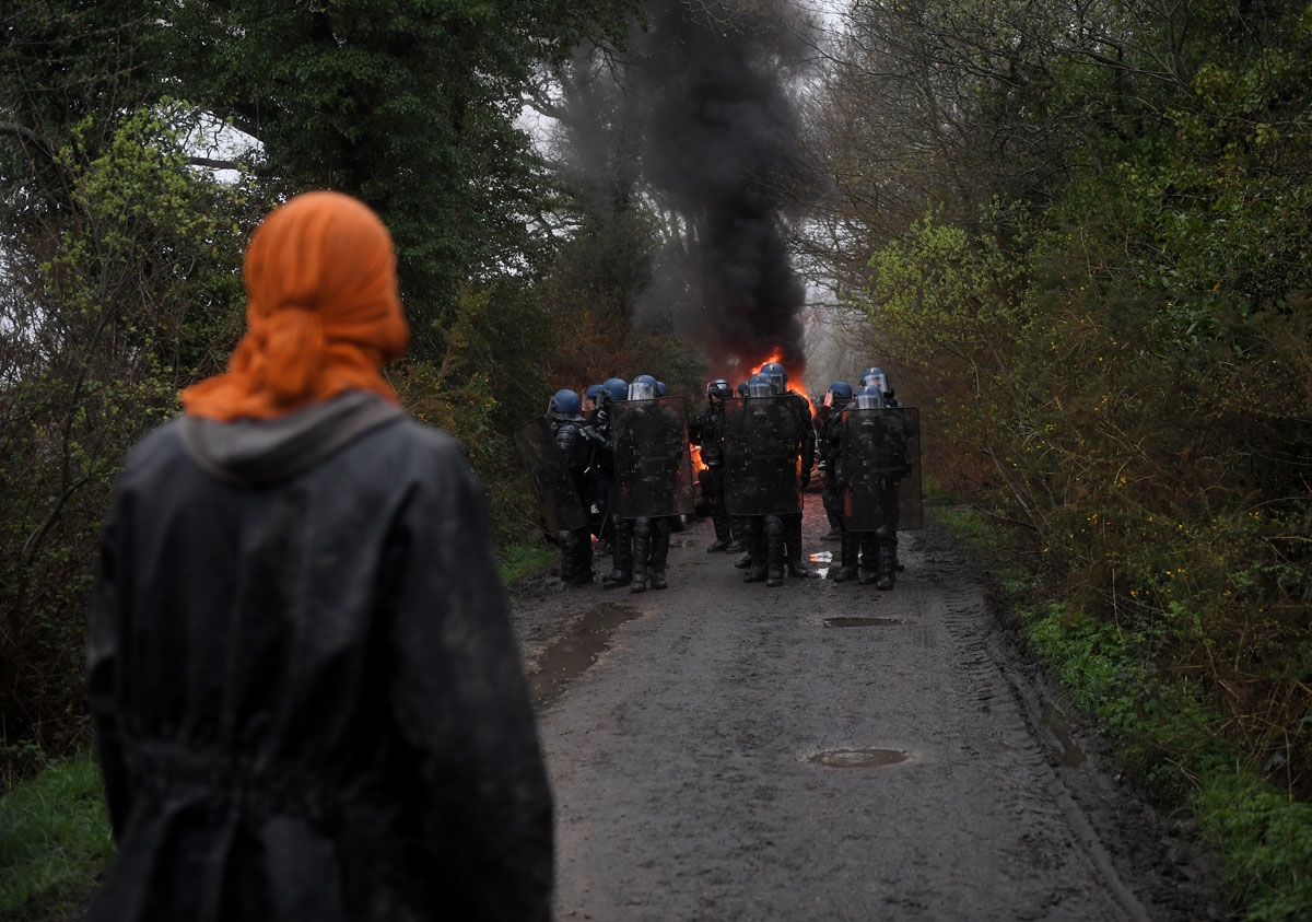 A protester looks towards a group of riot police during the eviction of environmental protesters from the site, known as ZAD (Zone a Defendre - Zone to defend) of what had been a proposed new airport in Notre dame des Landes on April 9, 2018.