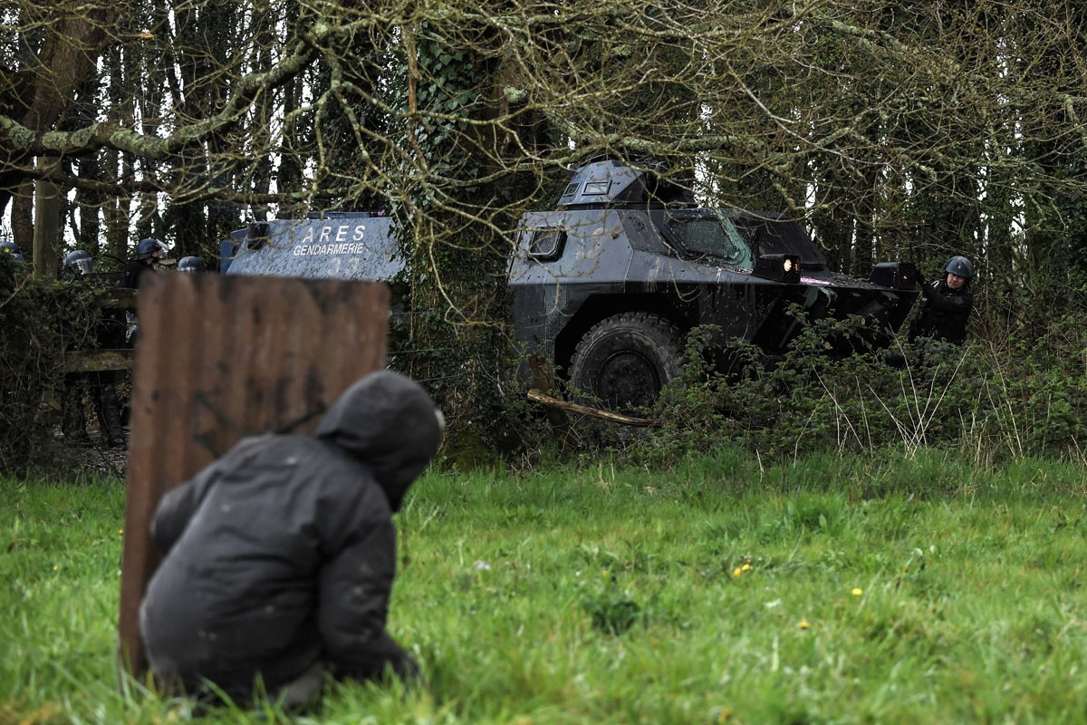 A protester behind a makeshift shield faces riot Gendarmes and their armoured vehicul on April 10, 2018 during a police operation to raze the decade-old camp known as ZAD (Zone a