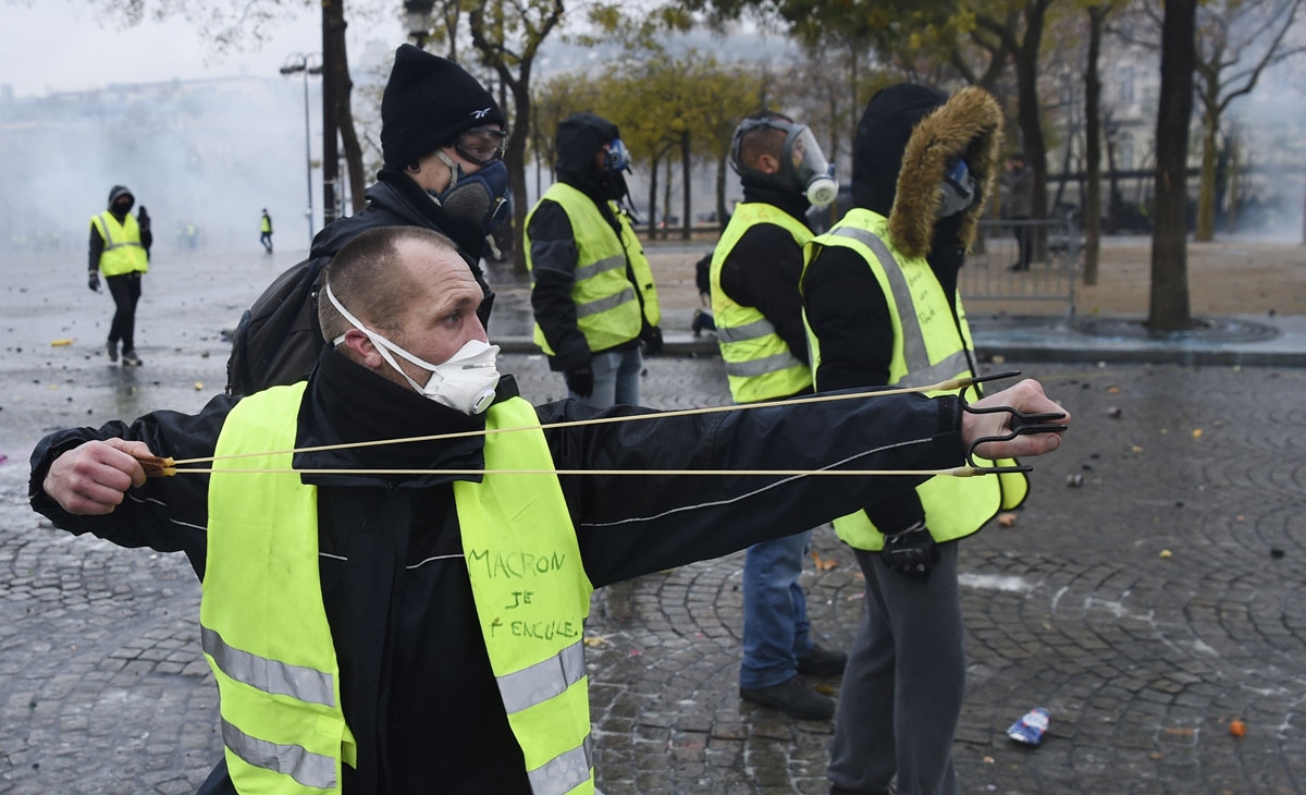 A demonstrator uses a slingshot to throw projectiles at police during a protest of Yellow vests (Gilets jaunes) against rising oil prices and living costs, on the Champs Elysees avenue in Paris on December 1, 2018. -