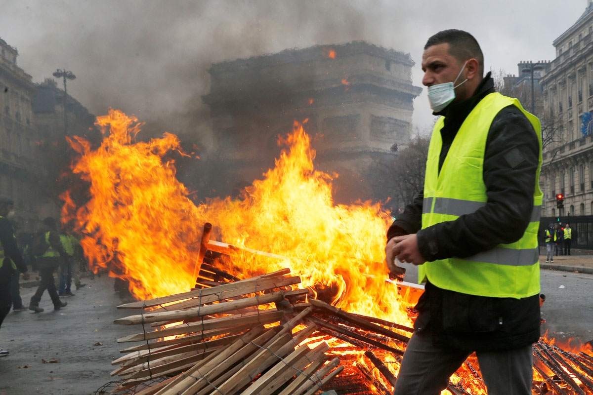 A demonstrator walks past a fire during a protest of Yellow vests (Gilets jaunes) against rising oil prices and living costs, near the Arc de Triomphe, in Paris, on December 1, 2018. - Thousands of anti-government protesters are expected on December 1, 20