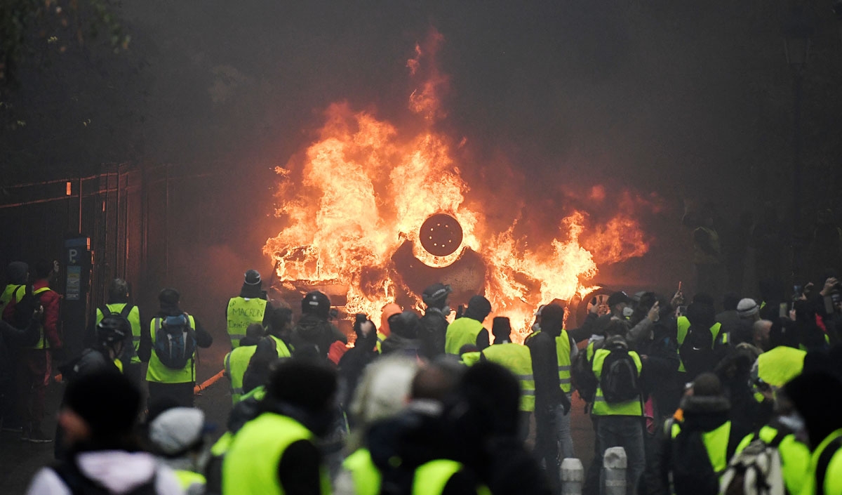 Demonstrators stand in front of a burning car during a protest of Yellow vests (Gilets jaunes) against rising oil prices and living costs, on December 1, 2018 in Paris.