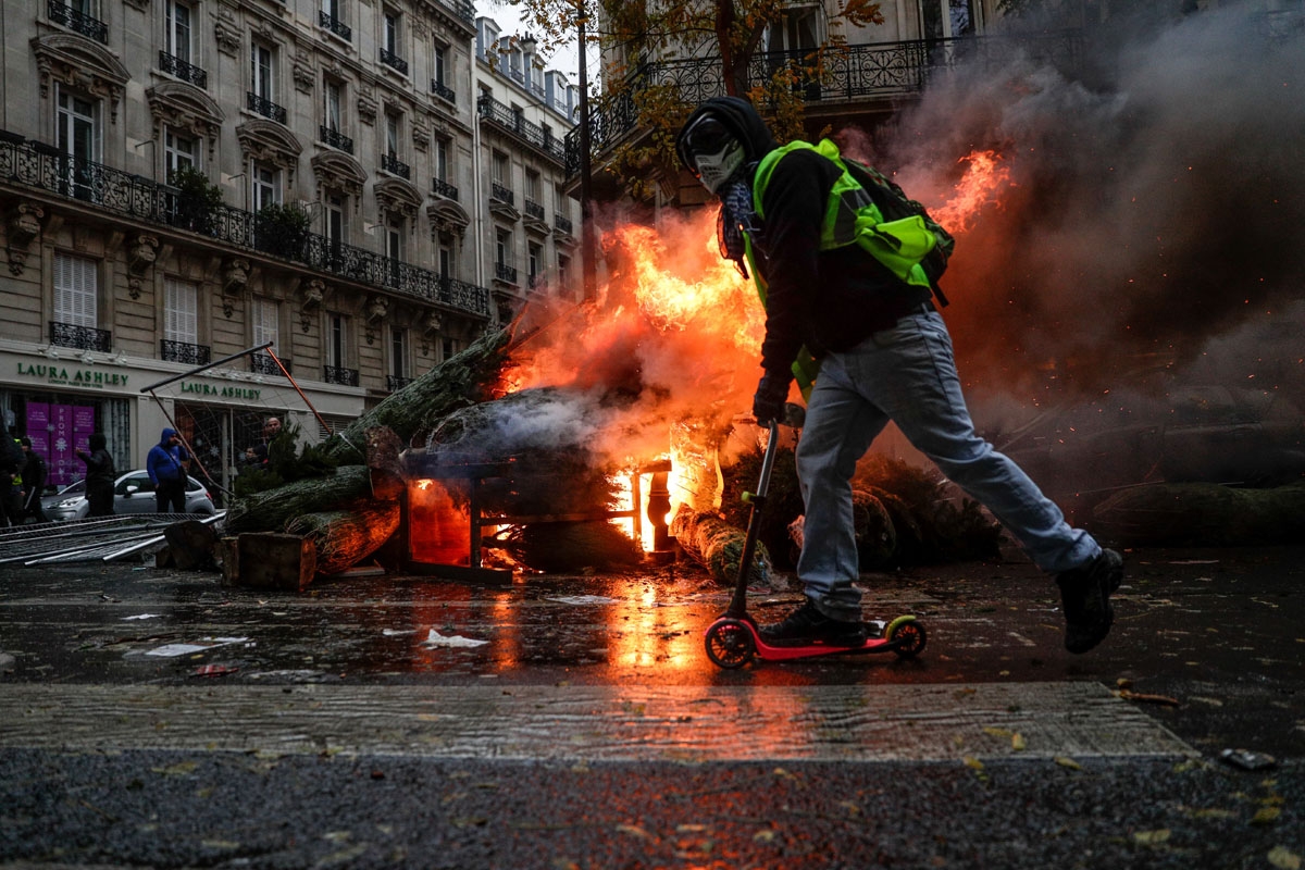 A demonstrator rides past a fire during a protest of Yellow vests (Gilets jaunes) against rising oil prices and living costs, on December 1, 2018 in Paris. - Speaking at the Paris police's command centre, French Prime Minister said 36,000 people were prot