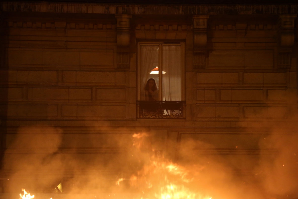A inhabitants looks at flames from her window during a demonstration by Yellow Vests (Gilets Jaunes in French) against rising oil prices and living costs, at Bastille in the French capital Paris on December 1, 2018.