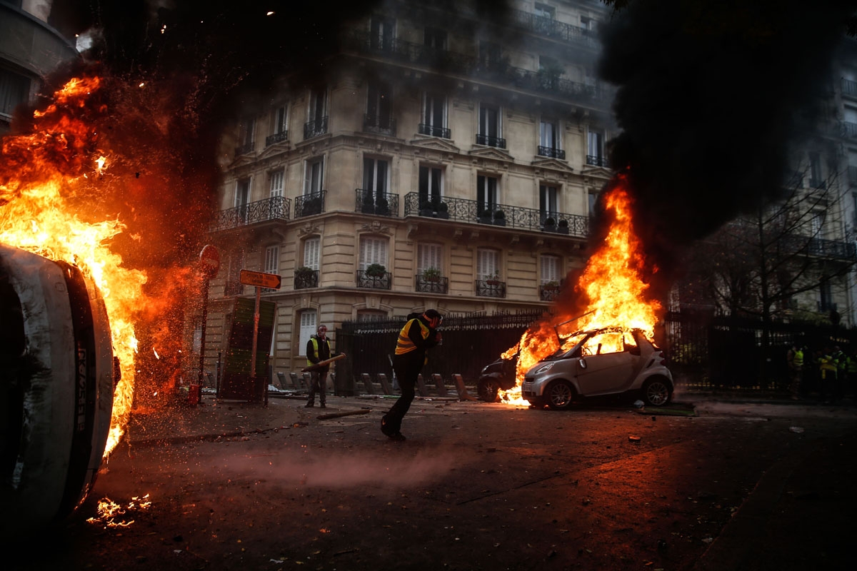 Protesters walk by burning cars during clashes with riot police on the sideline of a protest of Yellow vests (Gilets jaunes) against rising oil prices and living costs, on December 1, 2018 in Paris.