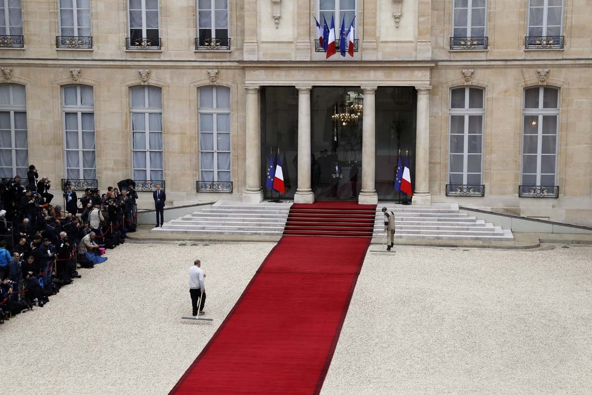 Employees rake the courtyard near the red carpet as journalists (L) wait at the entrance of the Elysee presidential Palace prior to the Emmanuel Macron's formal inauguration ceremony as French President on May 14, 2017 in Pari