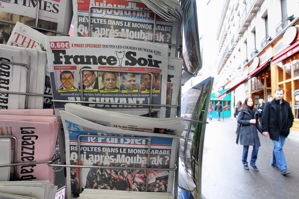 People are seen walking behind French daily newspapers displayed at a news kiosk on Februay 12, 2011 in Paris. The newspapers' covers are devoted to Egyptian Hosni Mubarak's overthrow and its consequences.
