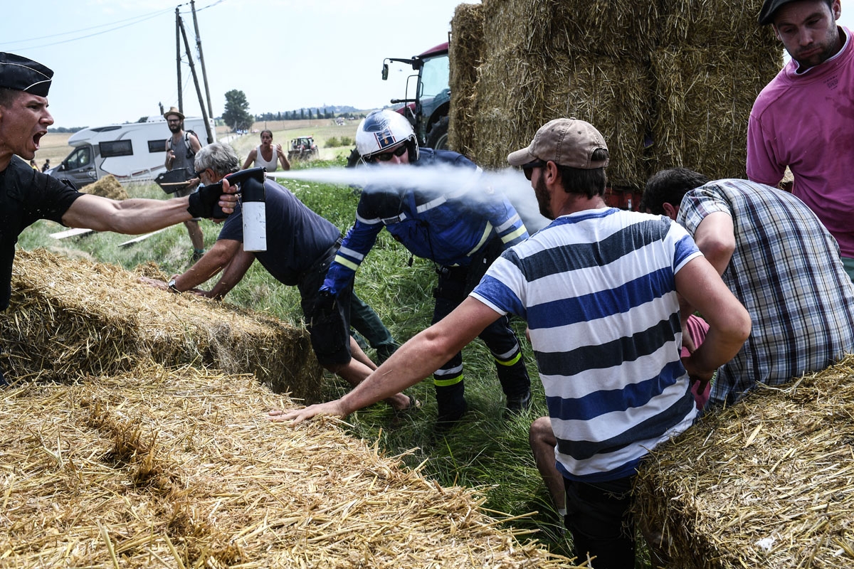 A gendarme (L) sprays tear gas at protesters (R) as other gendarmes remove haystacks from the route, during a farmers' protest who attempted to block the stage's route, during the 16th stage of the 105th edition of the Tour de France cycling race, between