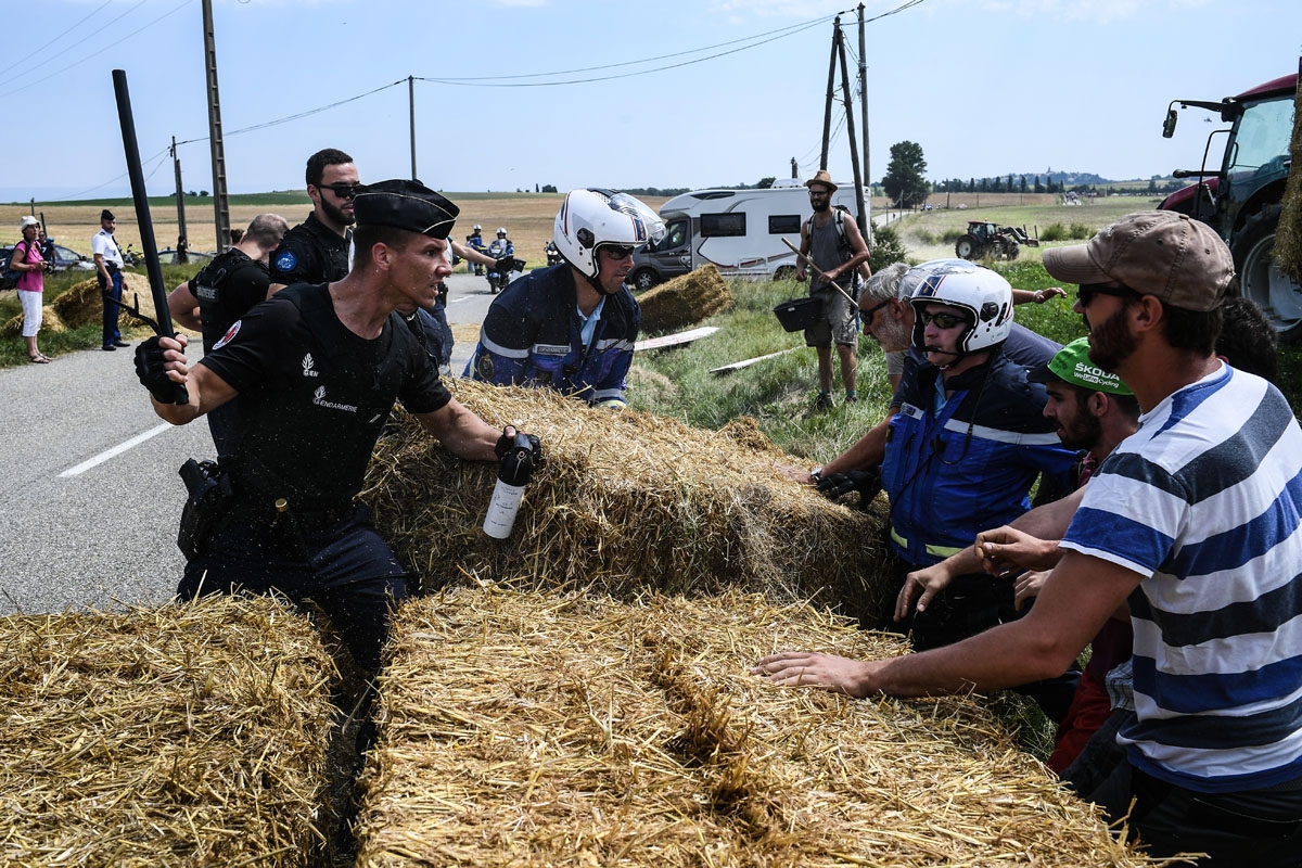 A gendarme (L) holding a baton and tear gas spray, holds back protesters (R) as other gendarmes remove haystacks from the route, during a farmers' protest who attempted to block the stage's route, during the 16th stage of the 105th edition of the Tour de