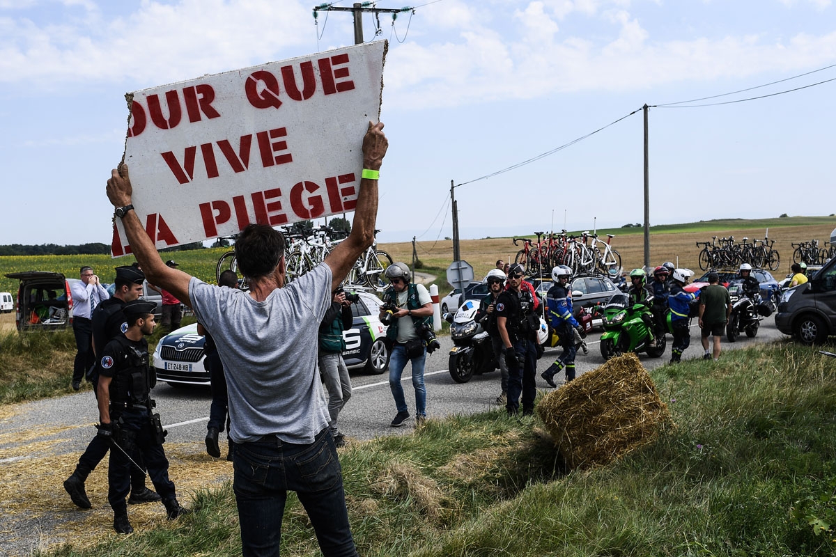 A protester holds a placard reading For the Piege region to live as gendarmes stand watch (Rear) during a farmers' protest who attempted to block the stage's route, during the 16th stage of the 105th edition of the Tour de France cycling race, between Car