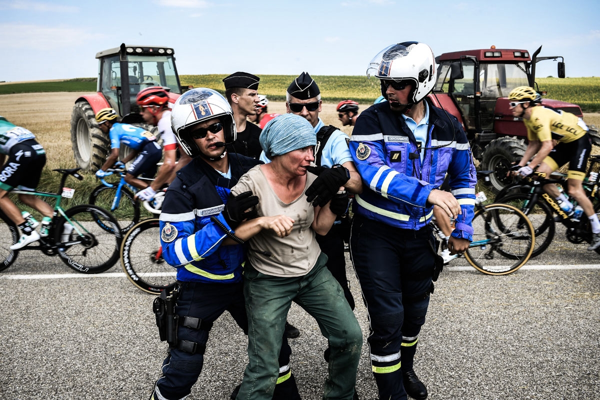 Gendarmes detain a protester as Great Britain's Geraint Thomas (R), wearing the overall leader's yellow jersey, and the pack ride behind, during a farmers' protest who attempted to block the stage's route, during the 16th stage of the 105th edition of the