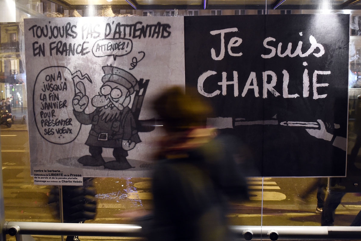 (FILES) This file photo taken on January 7, 2015 shows a woman walking by a poster bearing the last cartoon of late cartoonist Charb sticked on a bus station in Paris, following an attack by unknown gunmen on the offices of the satirical weekly, Charlie H