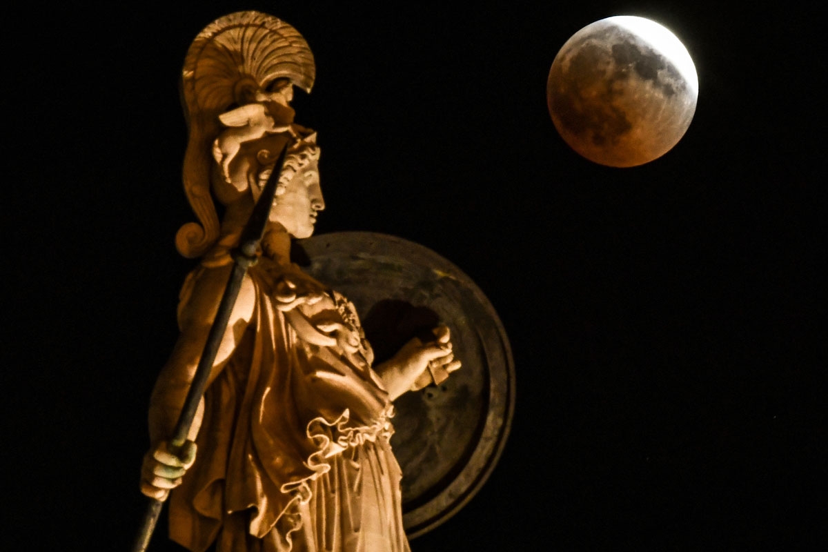 A picture shows the full moon during a blood moon eclipse beside a statue of ancient Greek goddess Athena in central Athens on July 27, 2018.