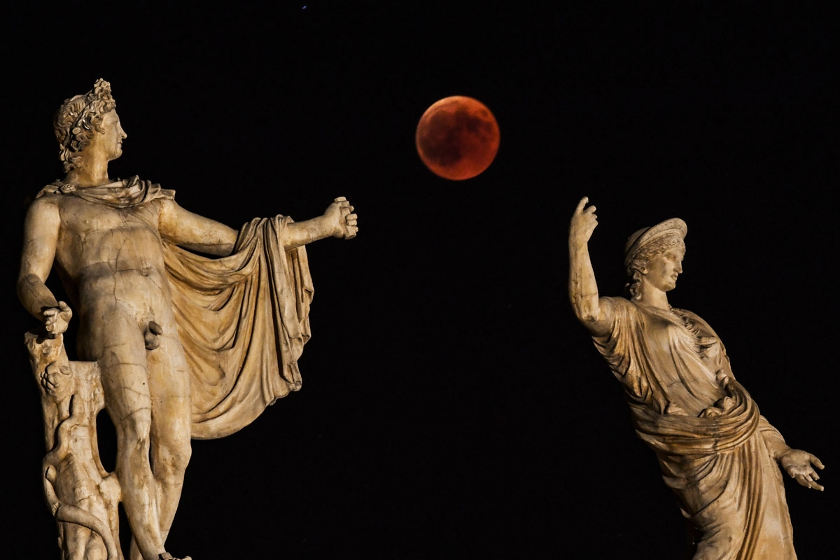 A picture shows the full moon during a blood moon eclipse beside a statue of ancient Greek goddes Hera (R) and god Apollo in central Athens on July 27, 2018.