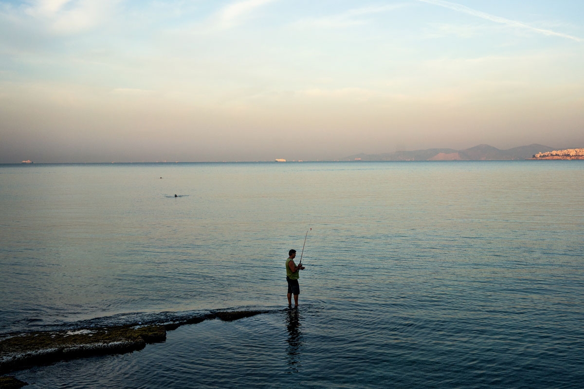 A man fishes off a rock on the beach of Faliro in Athens on October 2, 2016