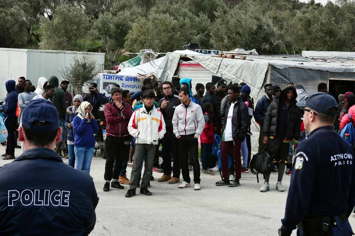 A picture taken on March 16, 2017 shows policemen standing guard near migrants at the Moria migrant camp on the island of Lesbos, almost a year after an EU-Turkey deal.