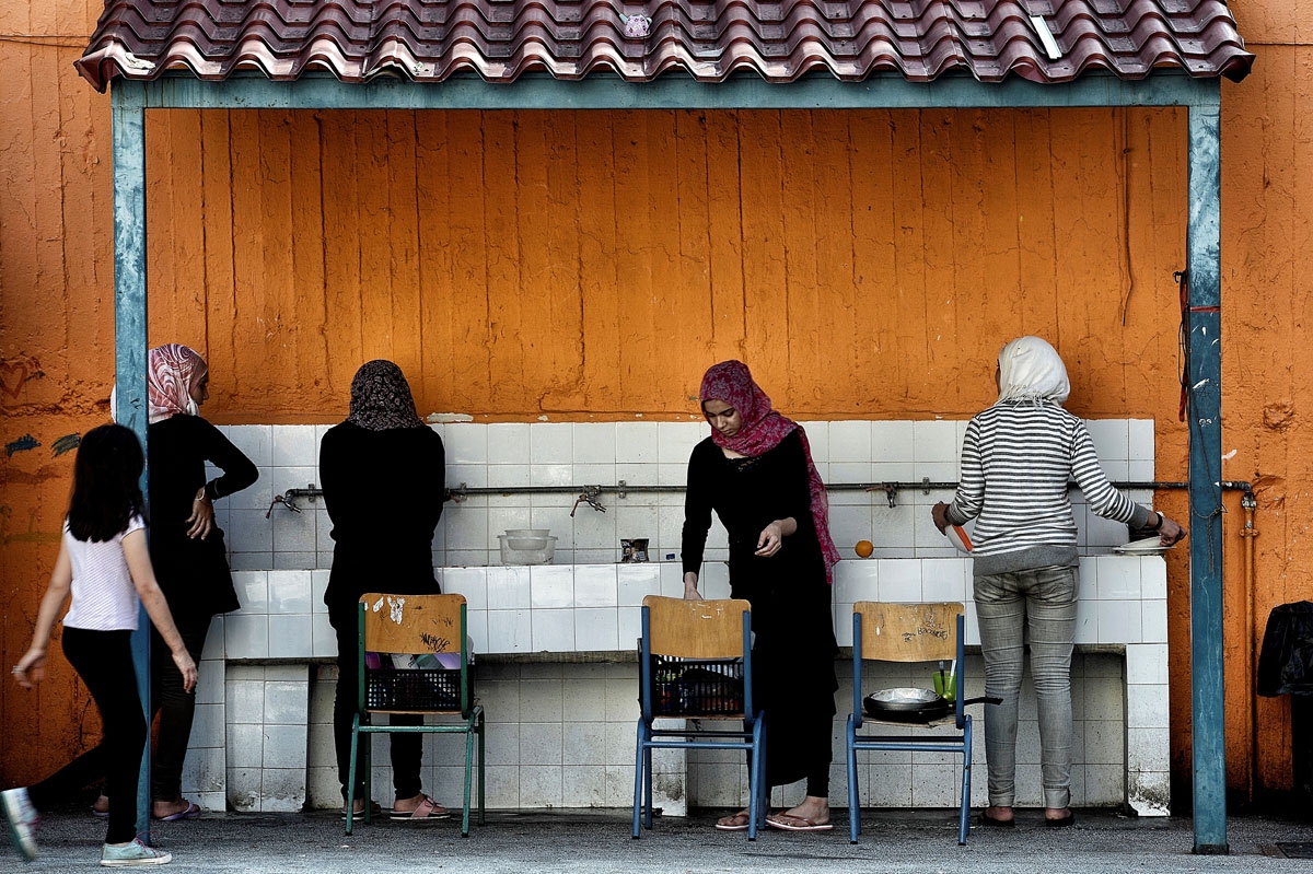 Women wash the dishes in the courtyard of an abandoned school used by volunteers for hosting Syrian and Afghan refugees in Athens on July 1, 2016.