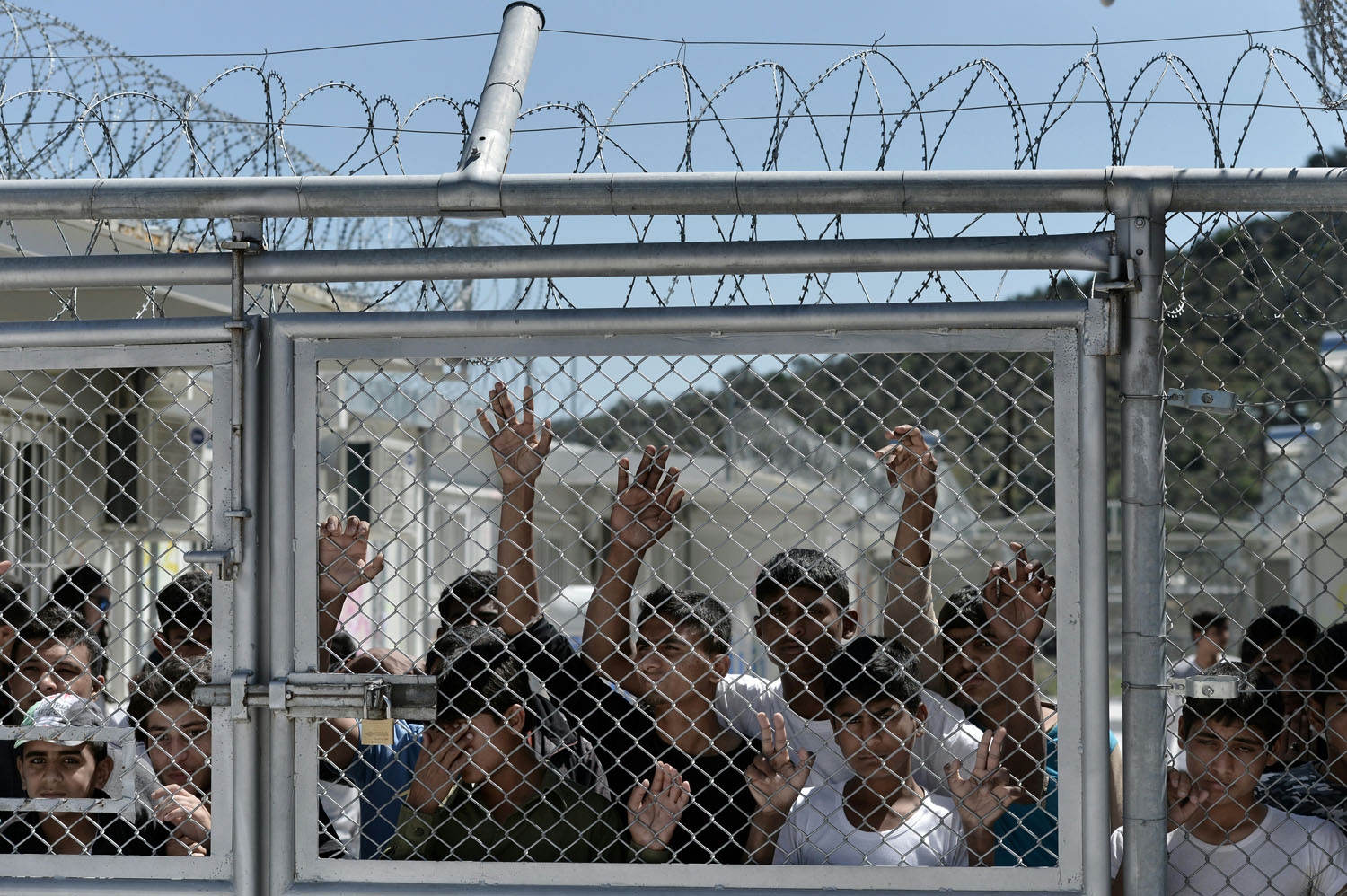 Young migrants and refugees stand at a fence of the Moria detention center during a visit of Pope Francis in Mytilene, on the Greek island of Lesbos, on April 16, 2016.