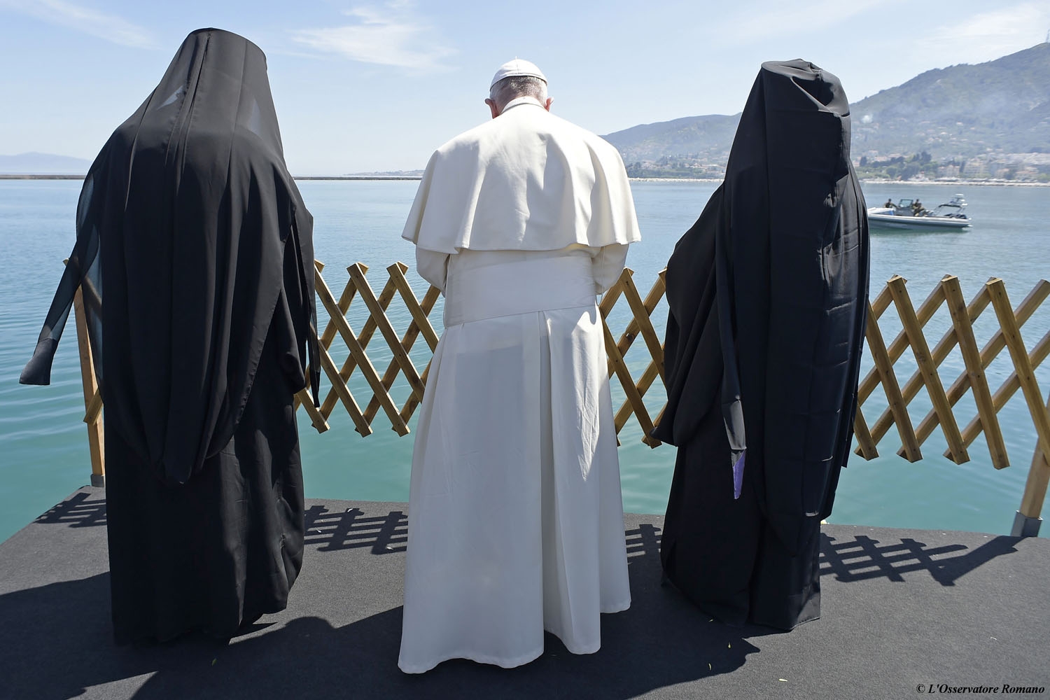 Pope Francis (C), Ecumenical Patriarch Bartholomew I, spiritual leader of the world’s Orthodox Christians (R) and Archbishop of Athens and All Greece Ieronymos II (L) pray after throwing wreaths of flowers in the port of Mytilene in memory of the migra