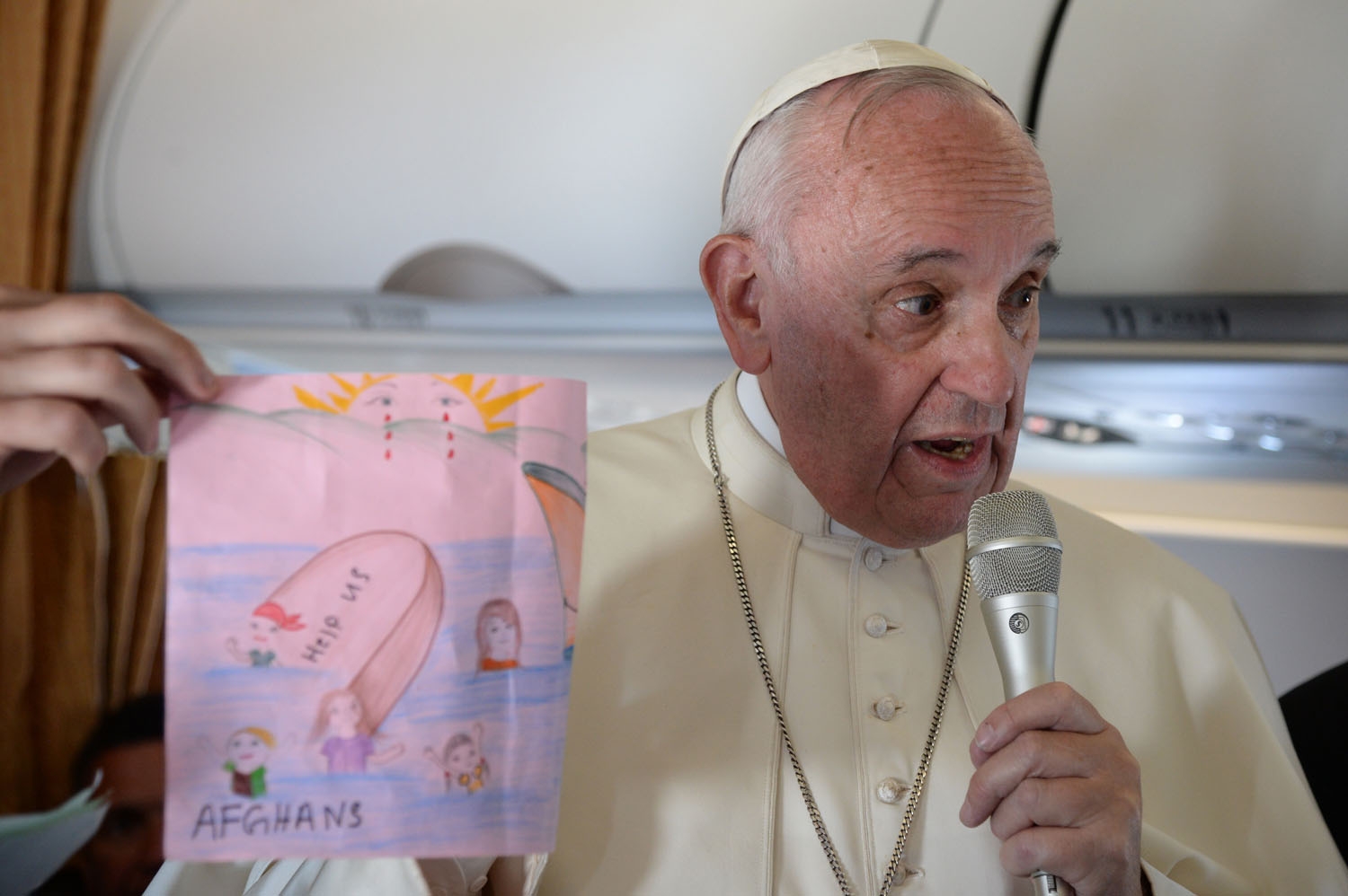 Pope Francis shows drawings made by children on his flight back to Rome following a visit at the Moria refugee camp on April 16, 2016 in the Greek island of Lesbos.