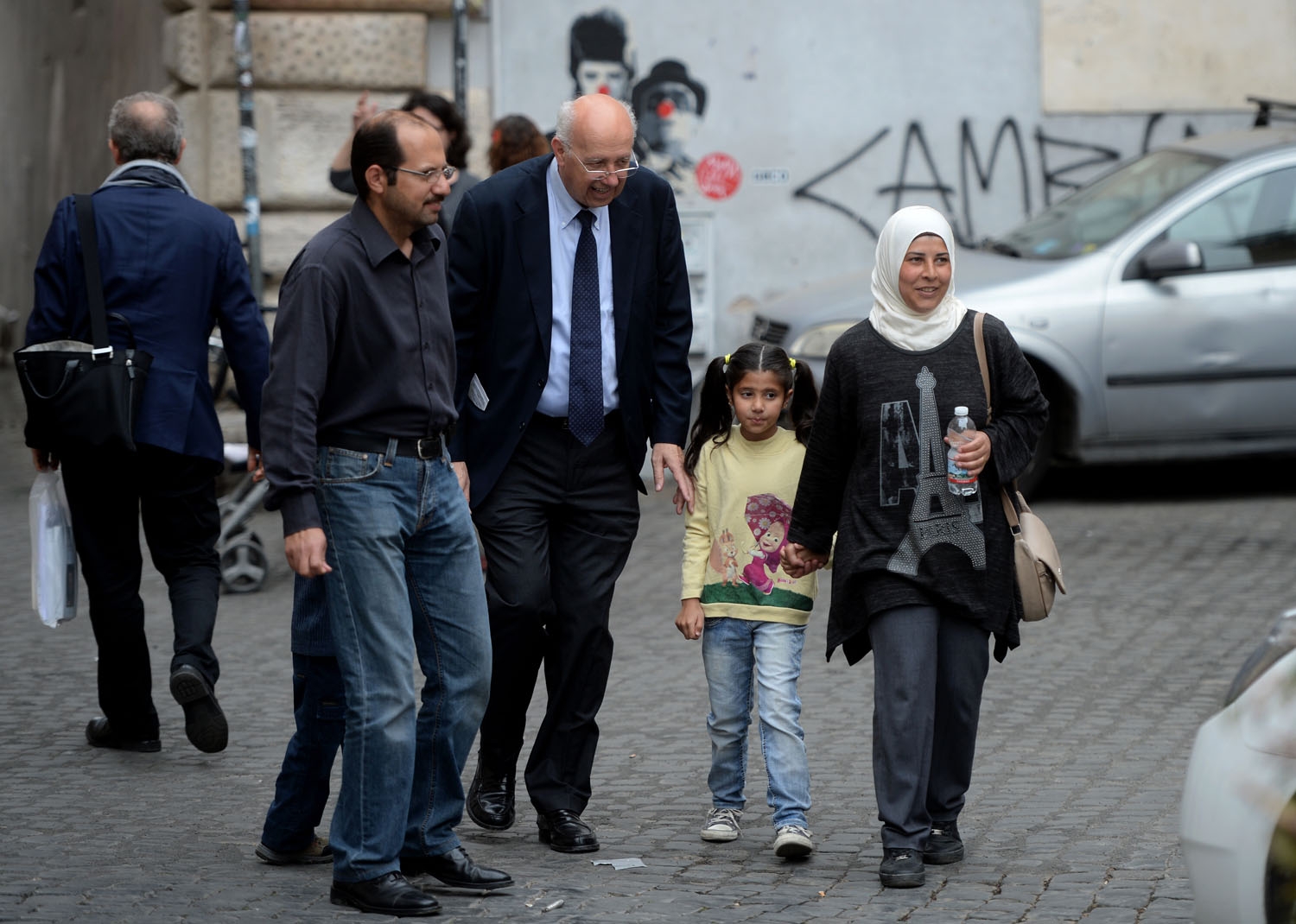 A family of Syrian refugees part of the 12 Syrian asylum seekers Pope Francis brought back with him from Greek island Lesbos, walk with a member of the St. Egidio Roman Catholic Charity (C), on April 18, 2016 in a street of Rome