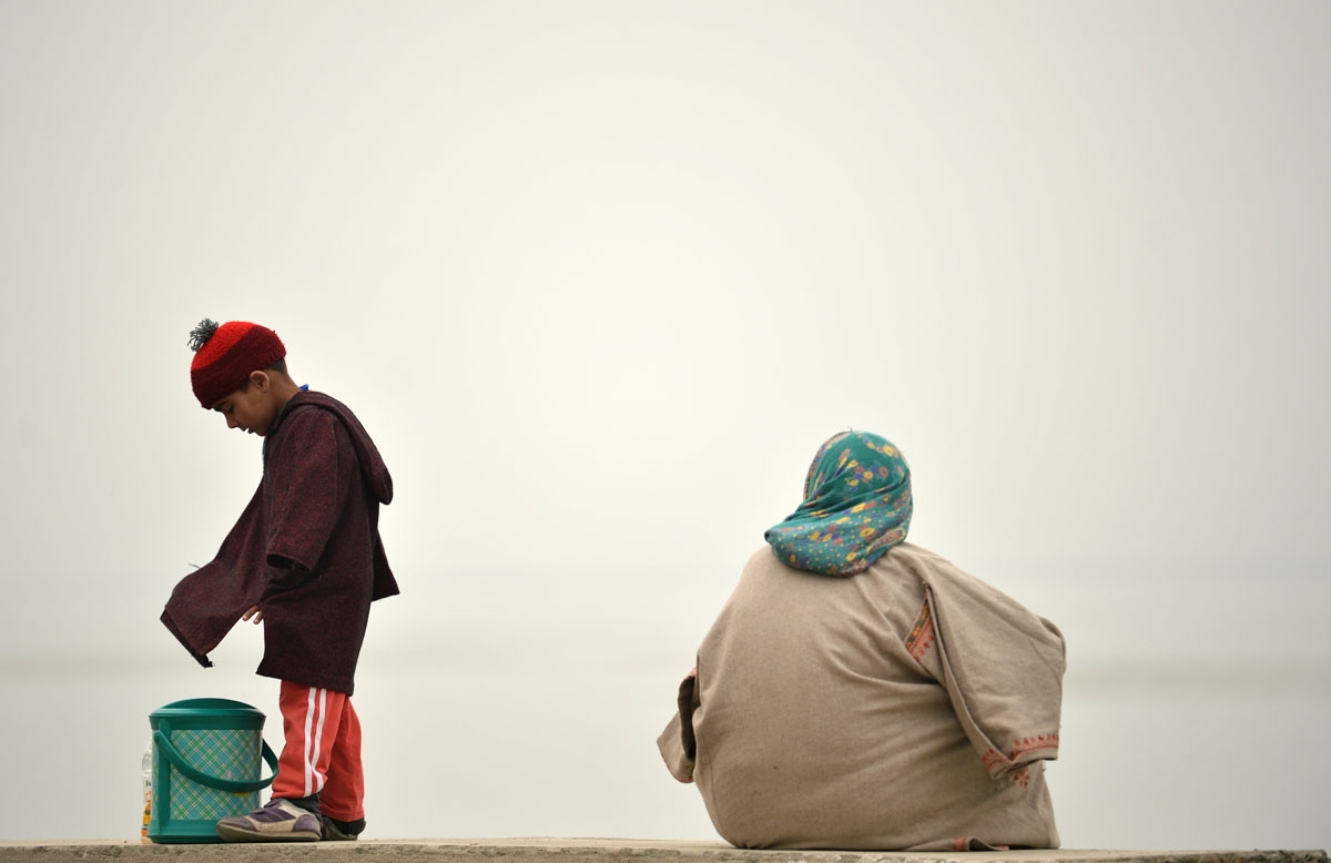 A woman sits on the shores of dal lake as her her play during a dense fog in Srinagar on November 20, 2016.