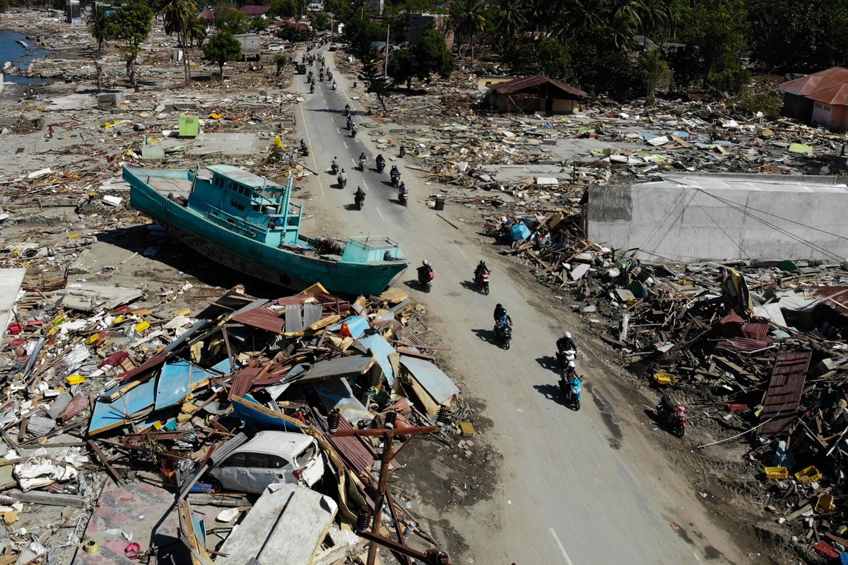 People drive past a washed up boat and collapsed buildings in Palu, Indonesia's Central Sulawesi on October 1, 2018, after an earthquake and tsunami hit the area on September 28. - The death toll from the Indonesian quake-tsunami nearly doubled to 832 bu