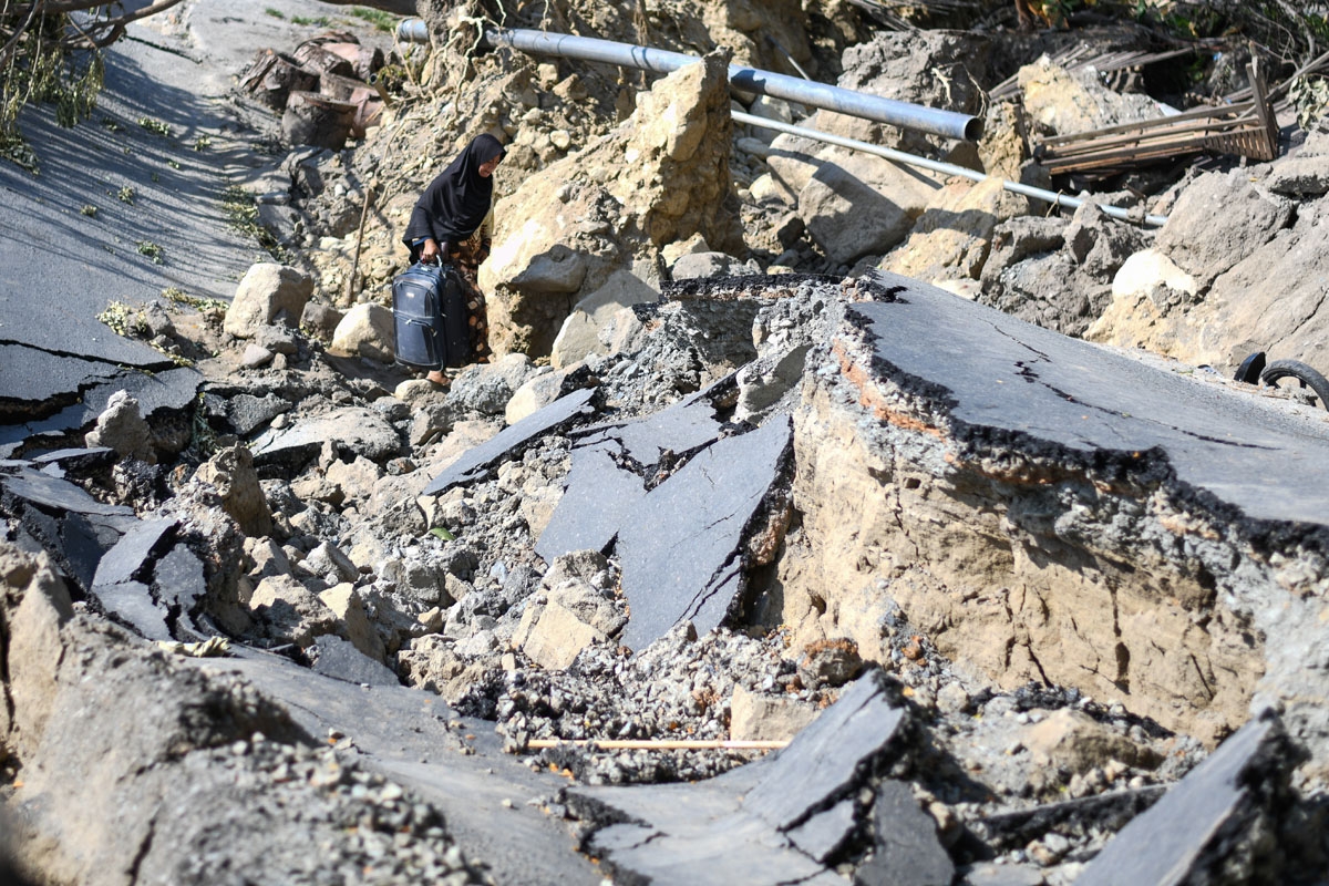 A woman with a suitcase makes her way along a destroyed road in Palu, Indonesia's Central Sulawesi on October 2, 2018.