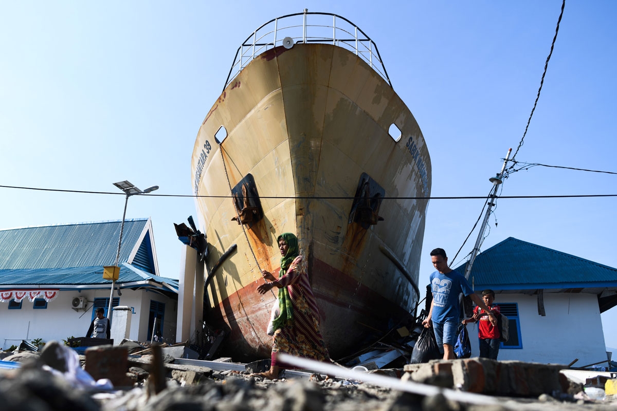 Quake survivors make their way past a washed out passenger ferry in Wani, Indonesia's Central Sulawesi on October 3, 2018, after an earthquake and tsunami hit the area on September 28. - Nearly 1,400 people are now known to have died in the quake-tsunami