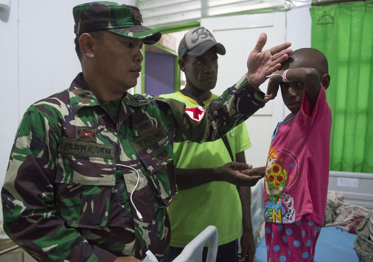A member of an Indonesian military task force checks a child at a local hospital in Agats, the capital of Asmat district in Indonesia's easternmost Papua province, on January 26, 2018.