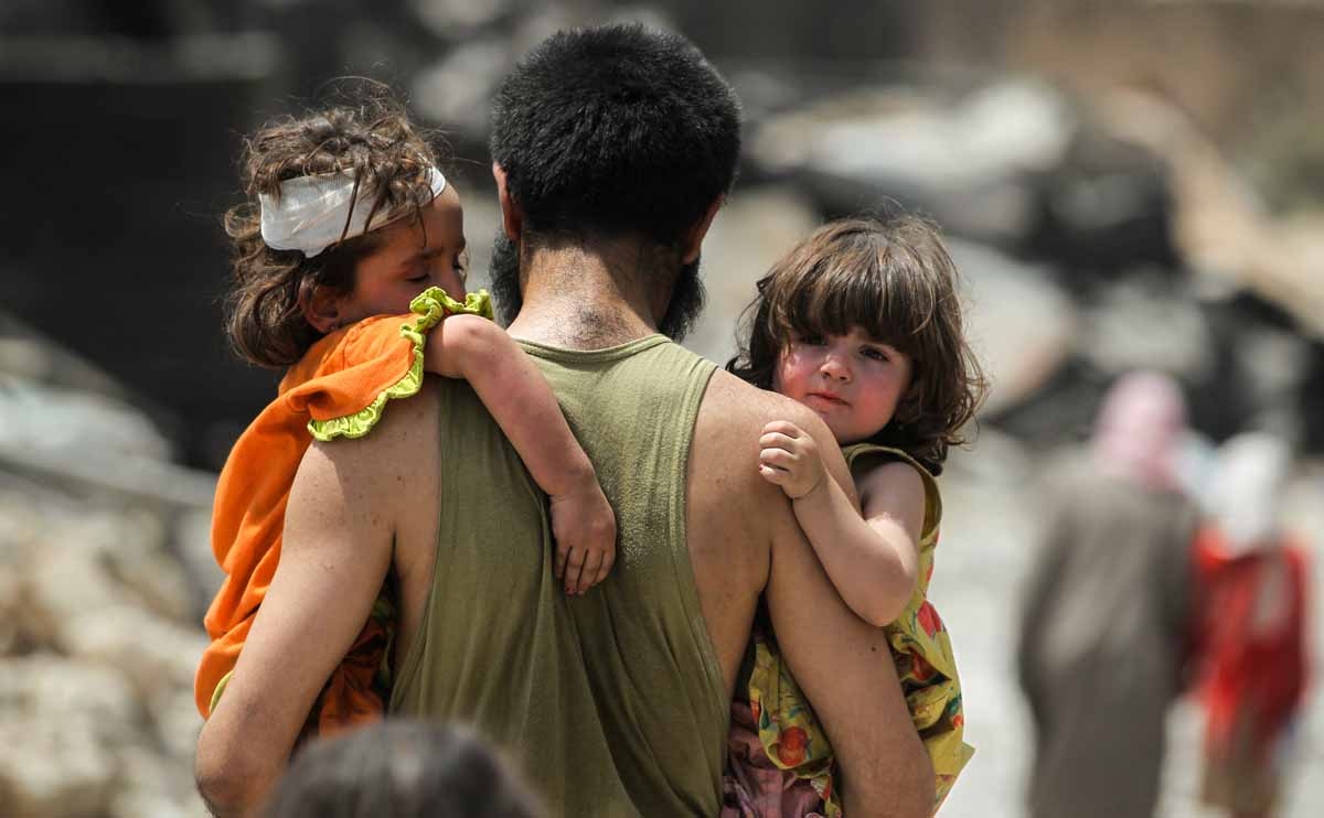 A man carries two children in his arms hile fleeing from the Old City of Mosul on July 2, 2017, as Iraqi government forces continue their offensive to retake the city from Islamic State (IS) group fighters.