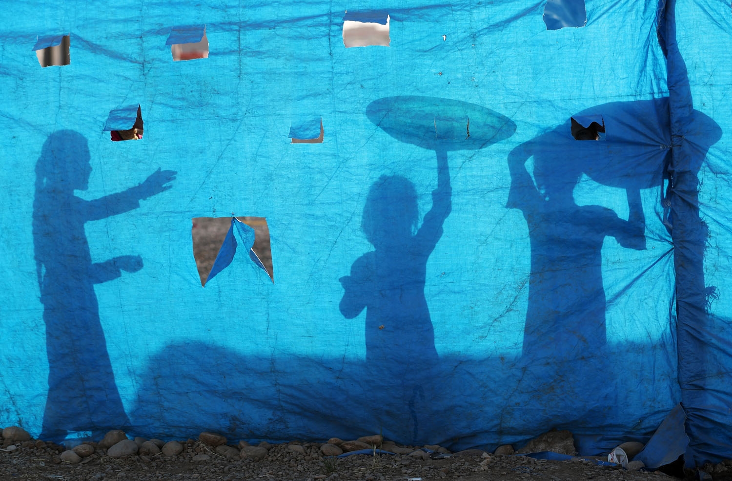 The silhouettes of Iraqi children are seen on tarpaulin as they collect water from a tank at the Al-Khazir camp for internally displaced people, located between Arbil and Mosul, on June 6, 2017.