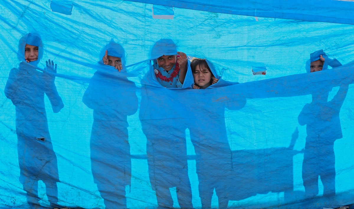 Iraqi children peer through a tarpaulin as they collect water from a tank at the Al-Khazir camp for internally displaced people, located between Arbil and Mosul, on June 6, 2017.