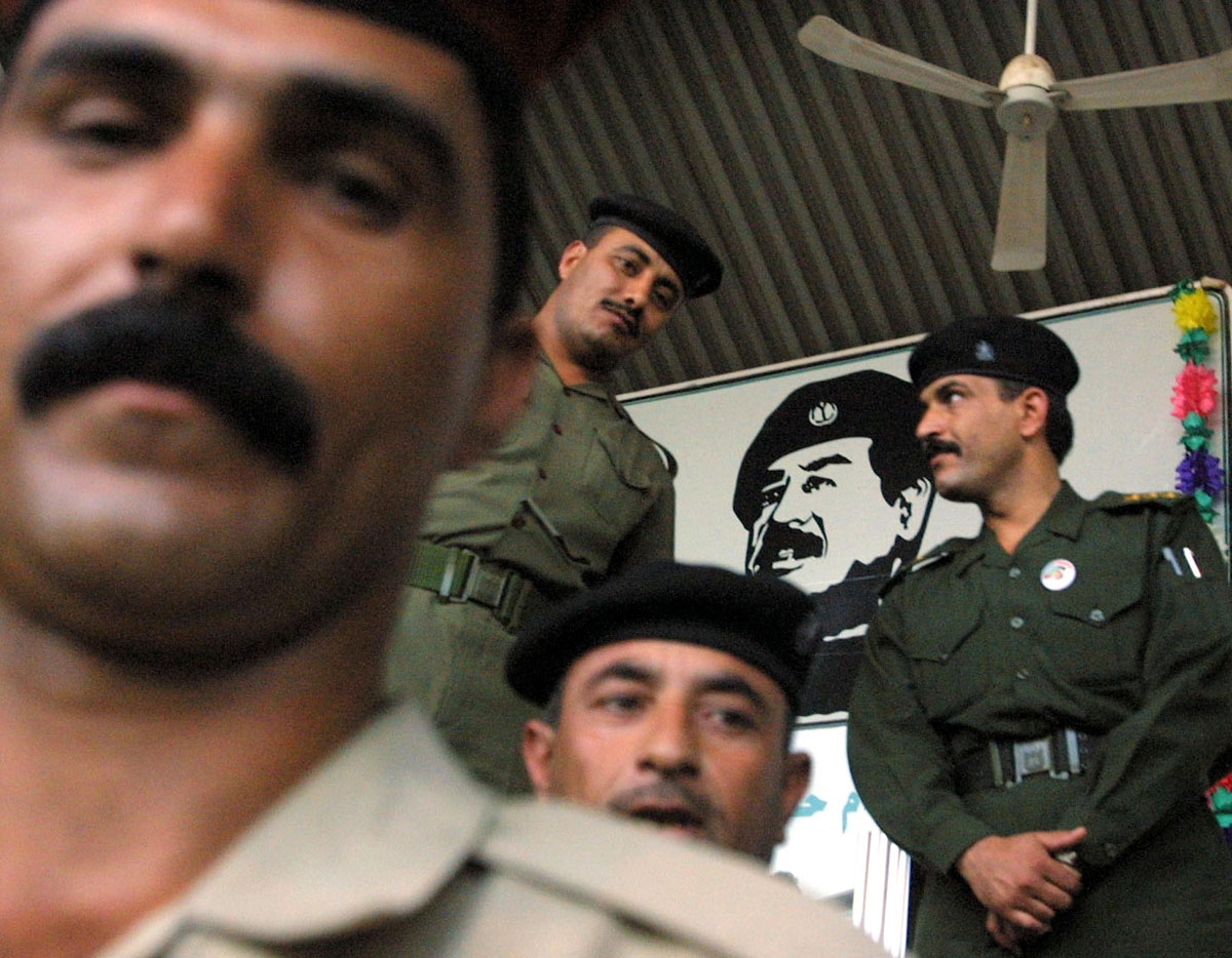 Iraqi officers stand under a huge portrait of President Saddam Hussein at Baghdad's National Stadium during a show in his support 14 October 2002. French Prime Minister Jean-Pierre Raffarin reiterated today that a military strike against Iraq must be a la