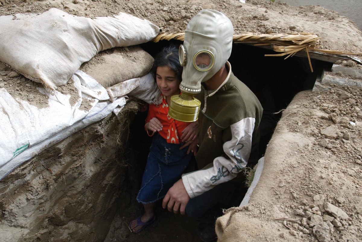 Iraqi Mustafa Mohammad, 13, wearing a WW II gas mask, plays with his sister Haya in a trench shored up by sandbags and bricks at their home garden in a Baghdad residential suburb 06 March 2003. Saddam made recently an appeal to his people to dig trenches