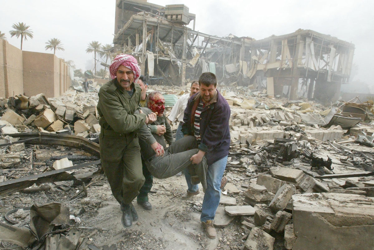 Iraqis carry an injured employee at the al-Salhiya telecomunications center after it was hit by a missile during a coalition air raid on Baghdad 30 March 2003. The raid took place as journalists were on a tour organized by the information ministry to be s