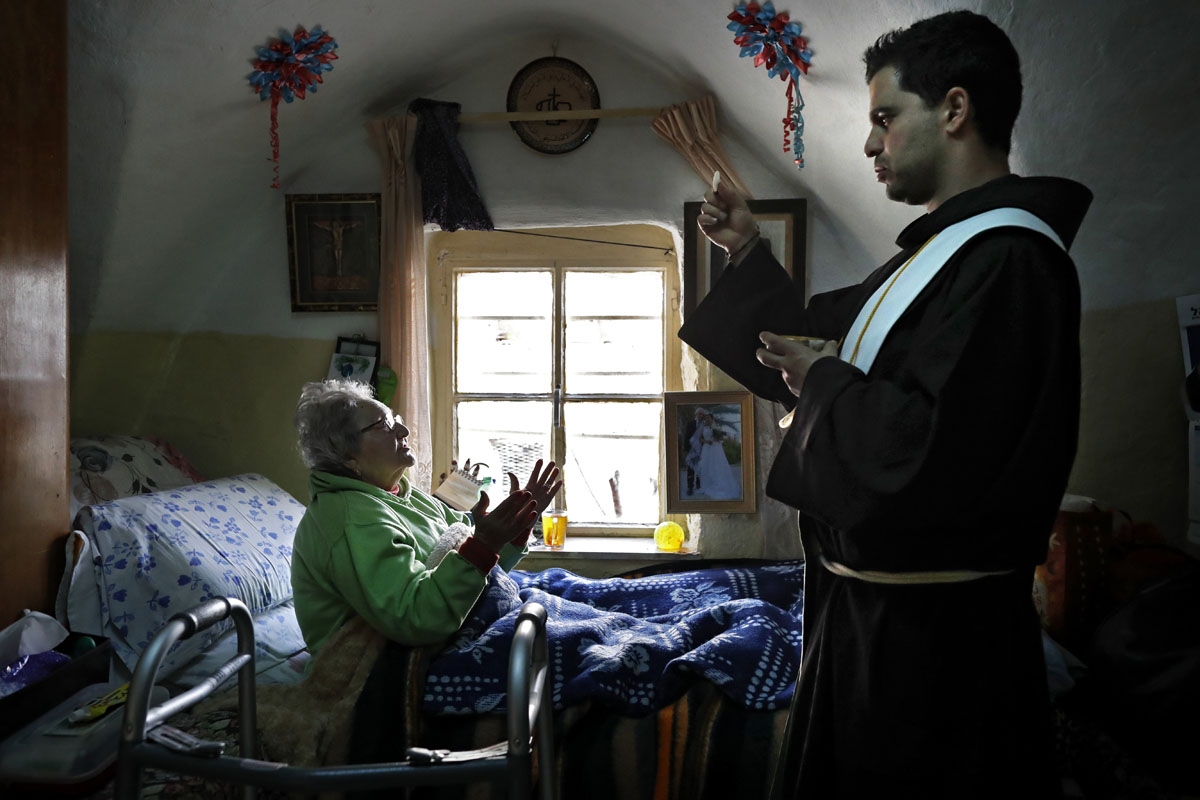 Franciscan friar Ayman Bathesh (R) gives communion to an elderly ill Christian woman at her home in the Old City of Jerusalem, on February 12, 2018.