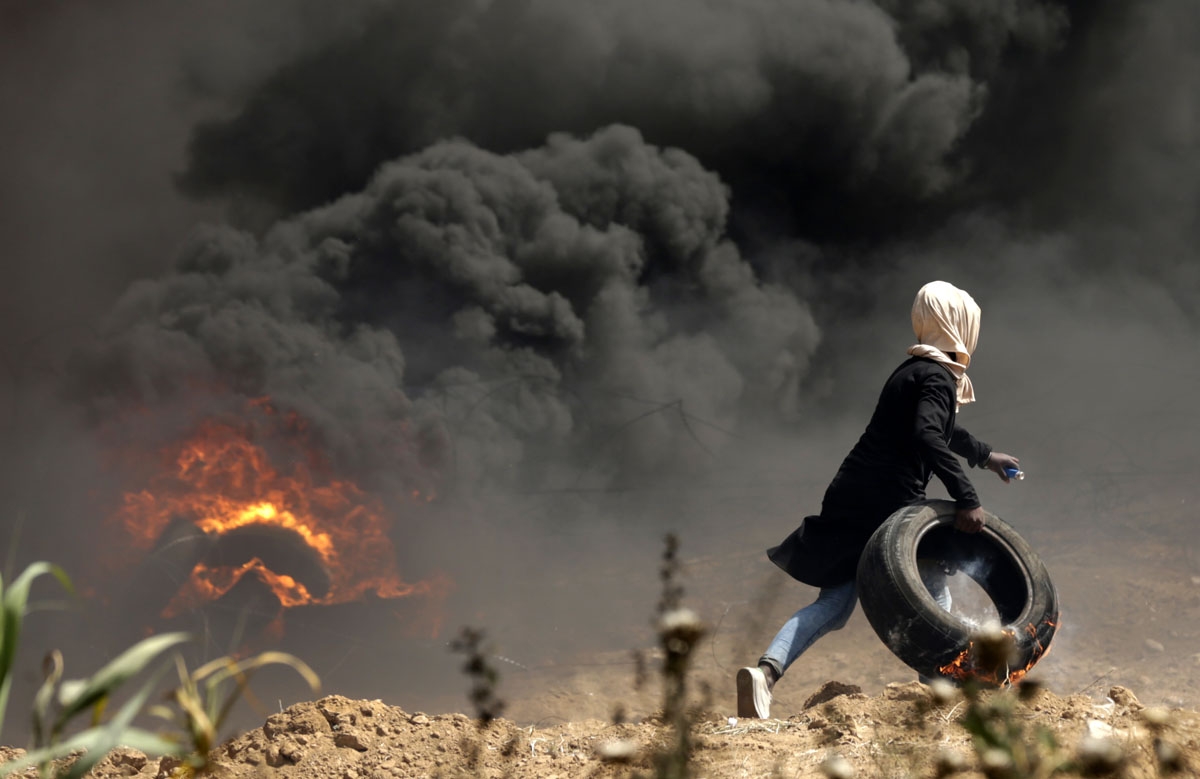 A Palestinian girl carries a tire in flames during clashes with Israeli security forces near the Israeli border fence, east of Gaza City in the central Gaza Strip on April 13, 2018. - Several thousand Gazans gathered for a third consecutive Friday of mass