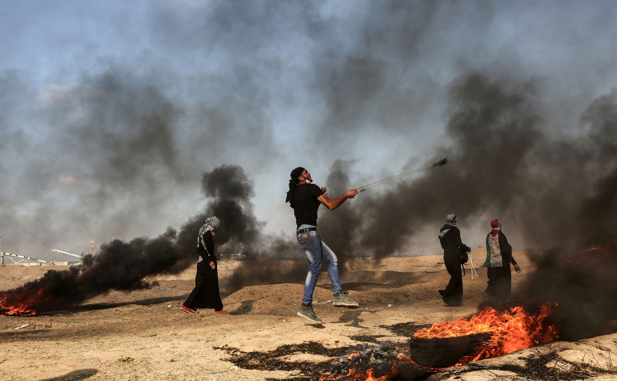 A Palestinian man uses a slingshot to throw a stone towards Israeli forces as smoke billows from burning tyres during a demonstration along the border with the Gaza strip east of Gaza city on June 1, 2018.
