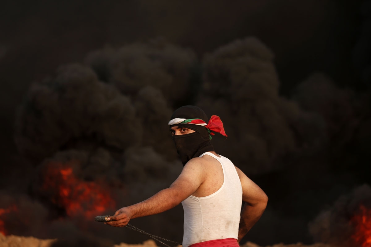A masked palestinian protester stands by smoke rising from burning tyres during a protest near the border with Israel east of Gaza City on August 31, 2018.