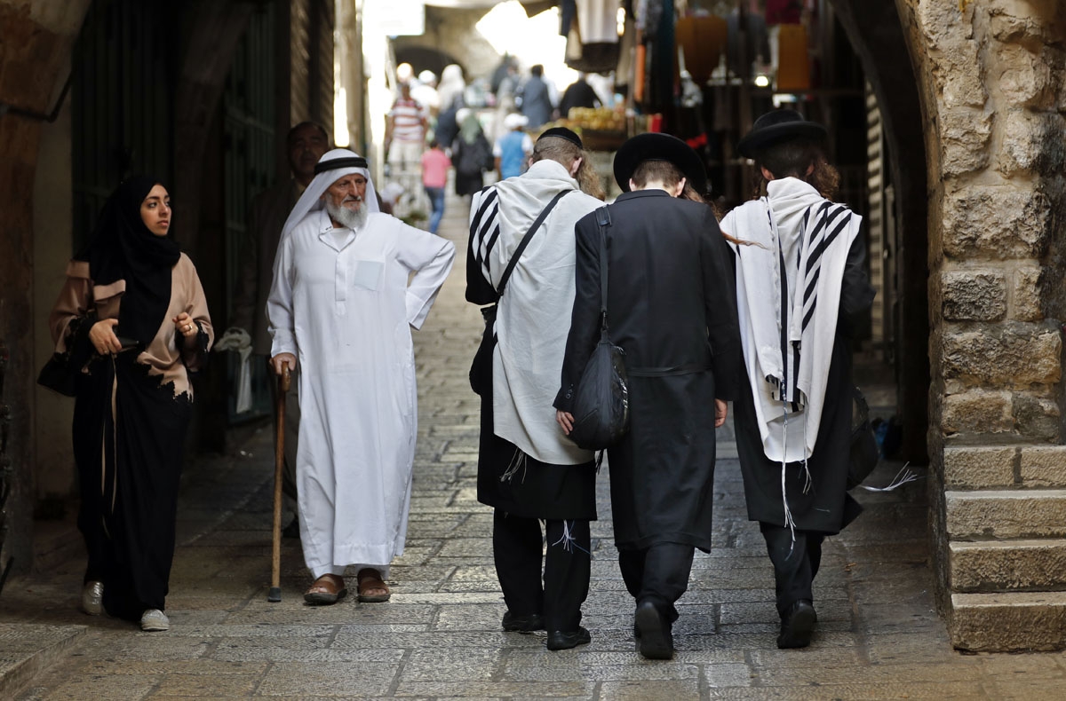 An elderly Palestinian man walks past a group of ultra Orthodox Jews in a street of Jerusalem's Old City on September 22, 2016.