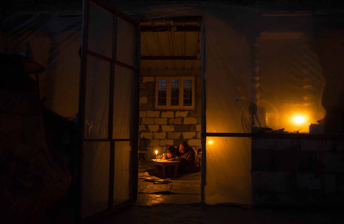 A Palestinian woman helps her son study by candlelight because of electricity shortages at their makeshift home in the Khan Yunis refugee camp in the southern Gaza Strip, April, 2017.