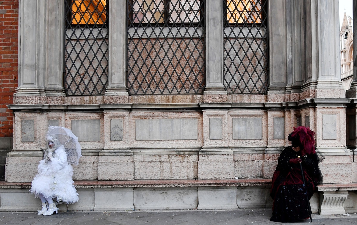 Masked people wearing traditional carnival costumes sit on a bench in Saint Mark Square in Venice, during Venice's Carnival on February 4, 2018.