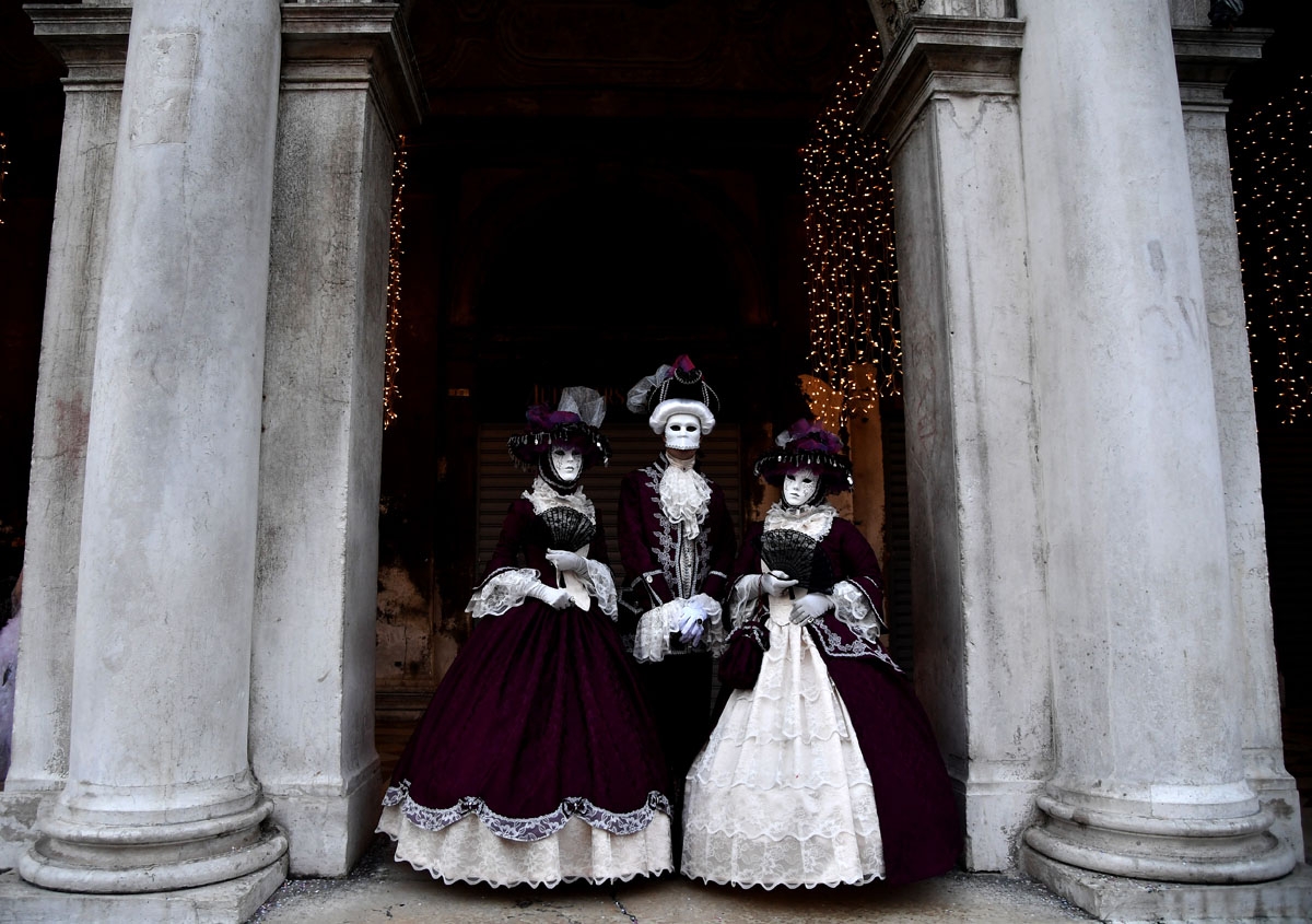A masked people wearing traditional carnival costumes pose in Saint Mark Square in Venice, during Venice's Carnival, on February 4, 2018. / A