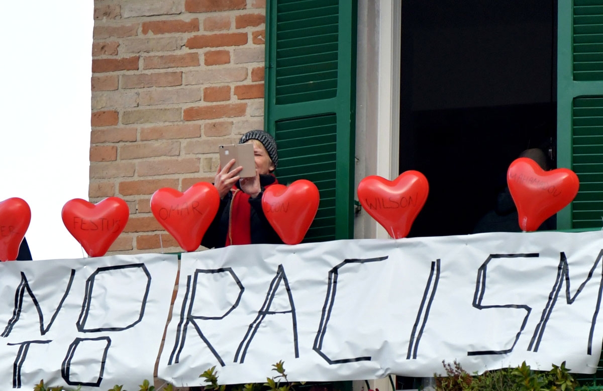 A woman stands on her balcony where she put red balloons with the victims' names and a banner reading no to racism during an anti-racism demonstration in the central Italian town of Macerata, on February 10, 2018, one week after an attack that injured at