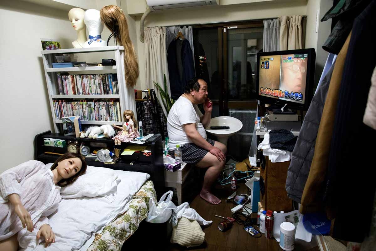 In this picture taken on April 20, 2017, 62-year-old Senji Nakajima speaks on his mobile phone as his silicone sex doll Saori (L) lies in bed at his apartment on the outskirts of Tokyo.